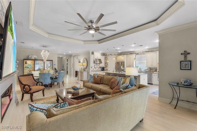 living room featuring a raised ceiling, ornamental molding, ceiling fan with notable chandelier, light hardwood / wood-style flooring, and sink