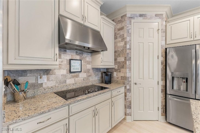 kitchen featuring stainless steel fridge, decorative backsplash, black electric cooktop, ornamental molding, and light stone counters