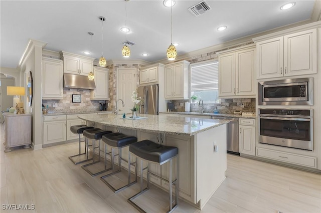 kitchen with a center island with sink, stainless steel appliances, hanging light fixtures, light stone counters, and a breakfast bar