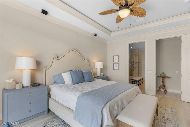 bedroom featuring ensuite bathroom, ceiling fan, a raised ceiling, crown molding, and light wood-type flooring