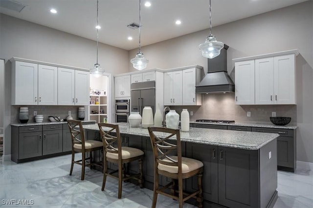 kitchen with appliances with stainless steel finishes, a center island, premium range hood, white cabinetry, and decorative light fixtures