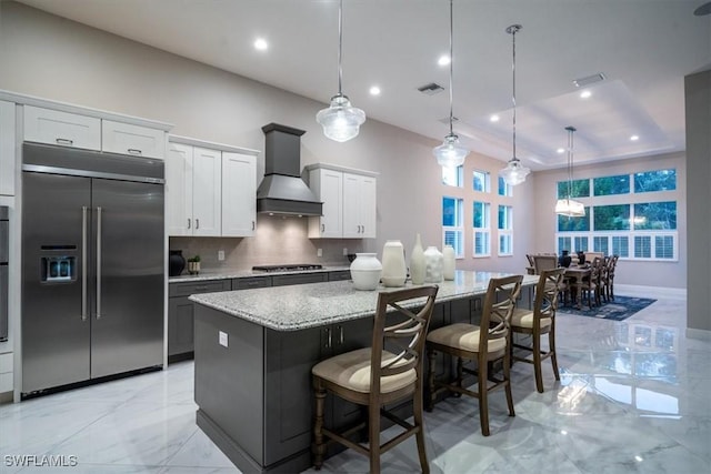 kitchen featuring custom exhaust hood, stainless steel appliances, a kitchen island, white cabinetry, and decorative light fixtures