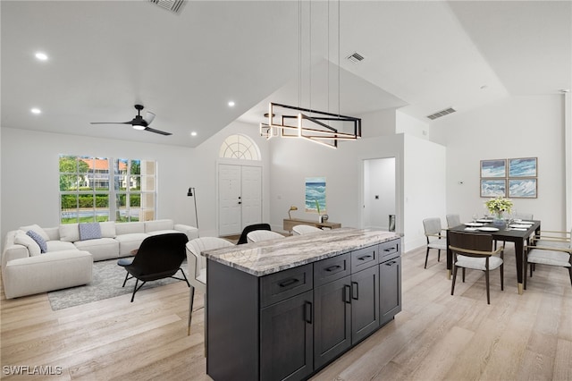 kitchen with light stone countertops, hanging light fixtures, light hardwood / wood-style floors, a kitchen island, and ceiling fan with notable chandelier