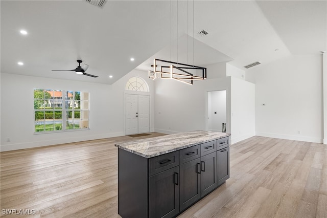 kitchen featuring lofted ceiling, ceiling fan with notable chandelier, hanging light fixtures, light stone countertops, and a kitchen island