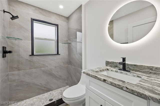 bathroom with a tile shower, vanity, and toilet