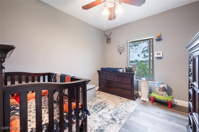 bedroom with ceiling fan, a nursery area, and light hardwood / wood-style floors