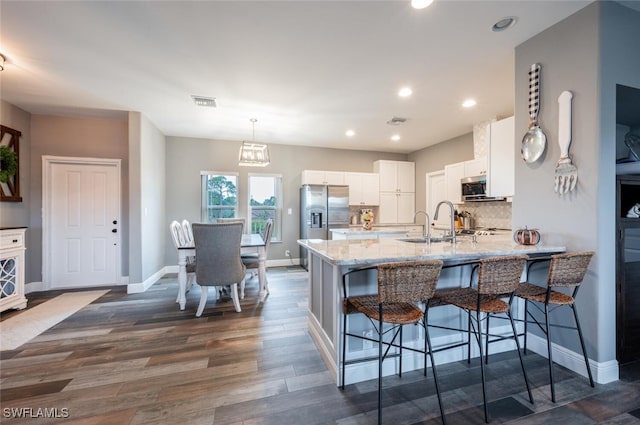 kitchen featuring a breakfast bar area, stainless steel appliances, decorative backsplash, hanging light fixtures, and white cabinets