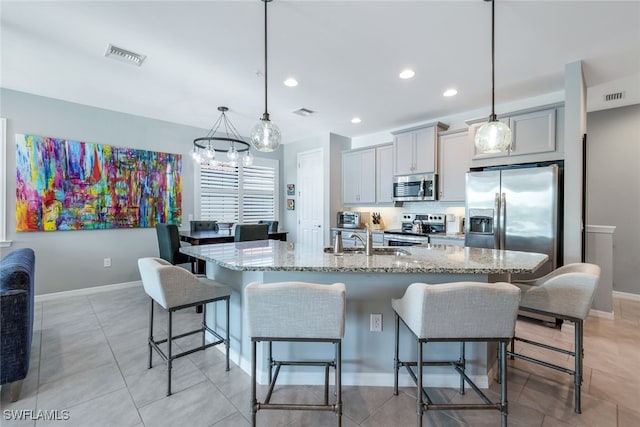 kitchen with decorative light fixtures, gray cabinets, a kitchen island with sink, and appliances with stainless steel finishes