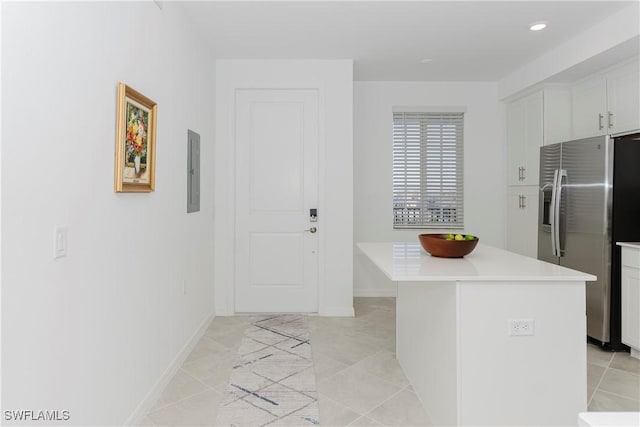 kitchen with white cabinetry, electric panel, light tile patterned floors, stainless steel fridge with ice dispenser, and a kitchen island