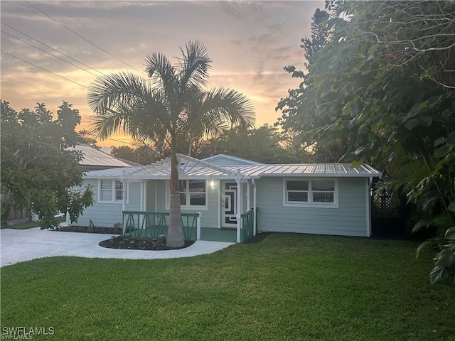 ranch-style home featuring covered porch, metal roof, and a front lawn