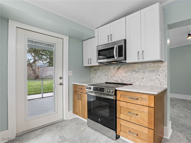 kitchen with tasteful backsplash, ornamental molding, stainless steel appliances, and white cabinetry