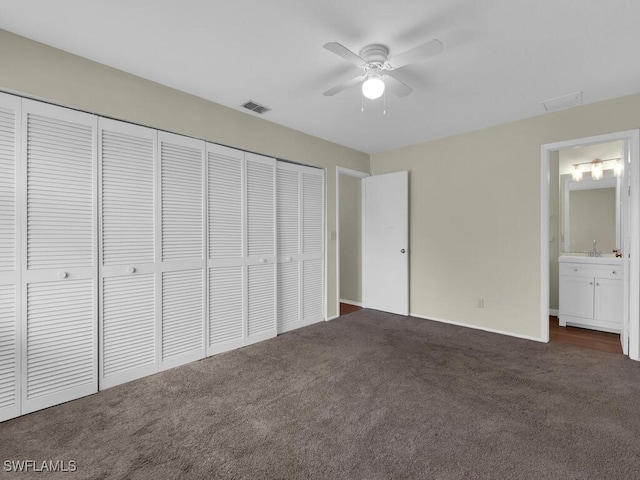 unfurnished bedroom with ensuite bathroom, sink, dark carpet, and a closet