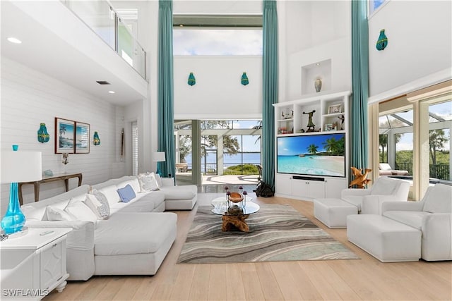 living room featuring a towering ceiling, a wealth of natural light, and light wood-type flooring