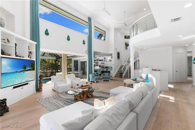 living room featuring a high ceiling, ceiling fan, and light wood-type flooring