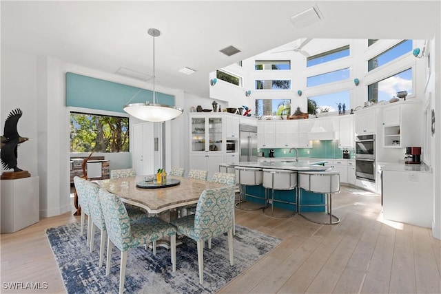 dining area with a towering ceiling, ceiling fan, and light hardwood / wood-style floors