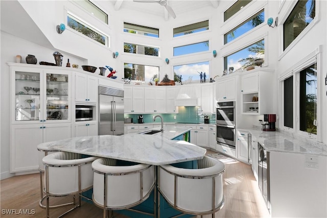 kitchen featuring stainless steel appliances, sink, white cabinetry, a towering ceiling, and a breakfast bar