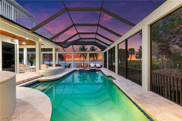 pool at dusk featuring a patio, glass enclosure, and an in ground hot tub