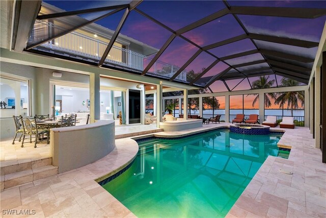 pool at dusk with a lanai, an in ground hot tub, and a patio