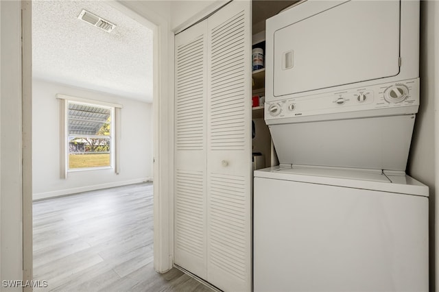 clothes washing area with stacked washer / drying machine, a textured ceiling, and light hardwood / wood-style flooring