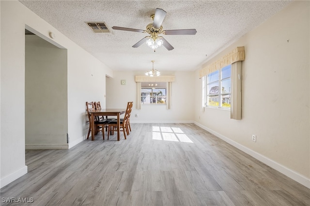 unfurnished dining area featuring ceiling fan with notable chandelier, a textured ceiling, and light hardwood / wood-style flooring