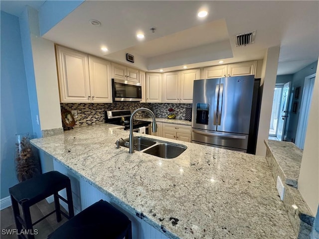 kitchen featuring kitchen peninsula, stainless steel appliances, backsplash, a breakfast bar area, and sink