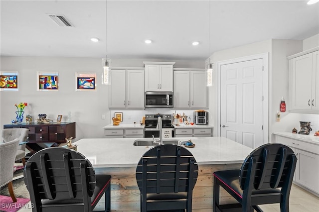 kitchen featuring a center island with sink, white cabinetry, stainless steel appliances, and pendant lighting