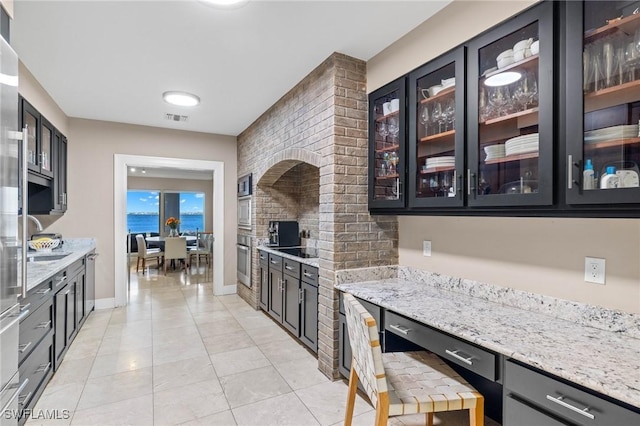 kitchen with stainless steel oven, light tile patterned flooring, a water view, light stone counters, and sink