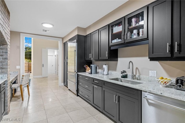 kitchen with light stone countertops, sink, light tile patterned floors, and dishwasher