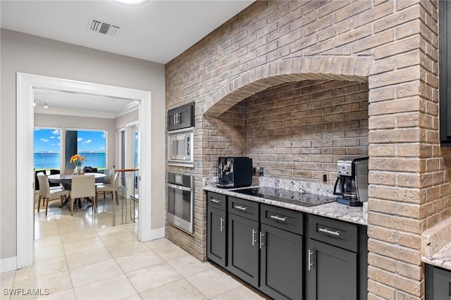 kitchen with brick wall, stainless steel appliances, a water view, light stone counters, and crown molding