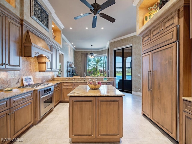 kitchen with stainless steel appliances, ornamental molding, custom range hood, light stone countertops, and a kitchen island