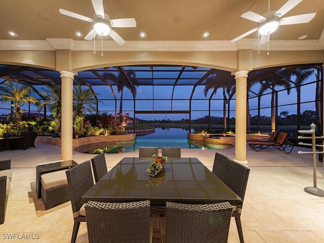 patio terrace at dusk featuring ceiling fan, glass enclosure, and a water view