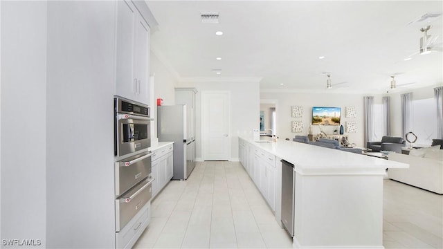 kitchen with sink, crown molding, a kitchen island with sink, stainless steel appliances, and white cabinets