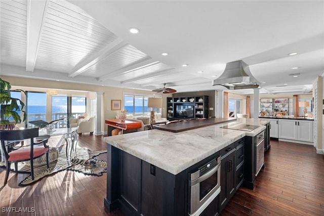 kitchen featuring light stone counters, beamed ceiling, ceiling fan, island exhaust hood, and dark wood-type flooring