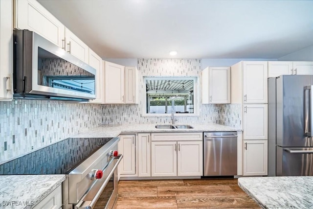 kitchen featuring light stone countertops, white cabinets, appliances with stainless steel finishes, wood-type flooring, and sink