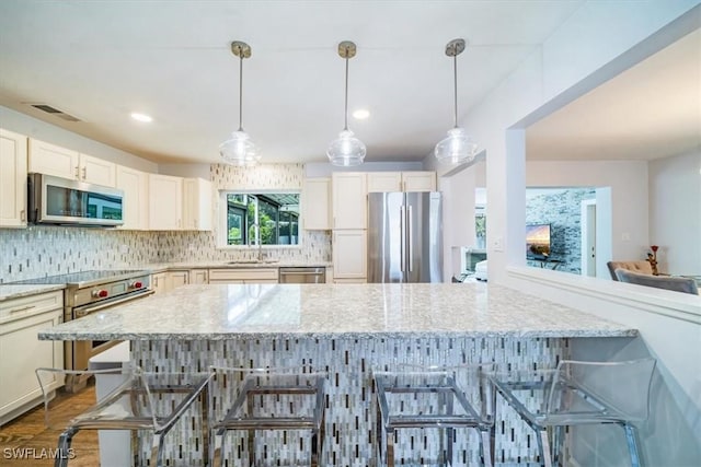 kitchen featuring decorative light fixtures, a breakfast bar, light stone counters, and appliances with stainless steel finishes