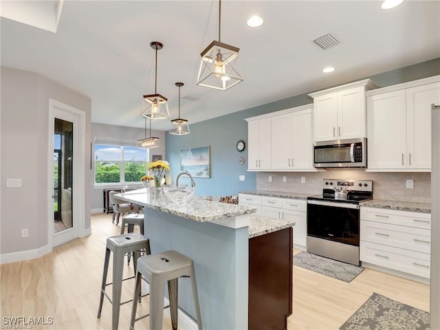 kitchen featuring stainless steel appliances, white cabinetry, an island with sink, backsplash, and hanging light fixtures