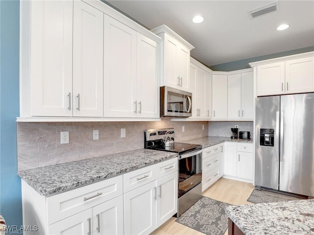 kitchen featuring appliances with stainless steel finishes, white cabinetry, light stone counters, and tasteful backsplash