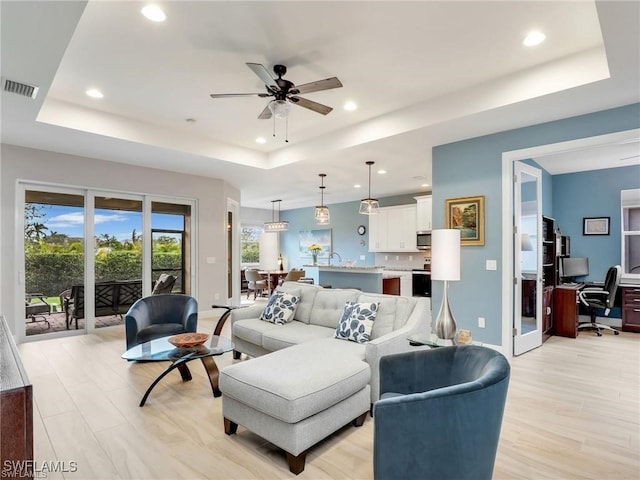 living room with ceiling fan, light hardwood / wood-style flooring, and a raised ceiling