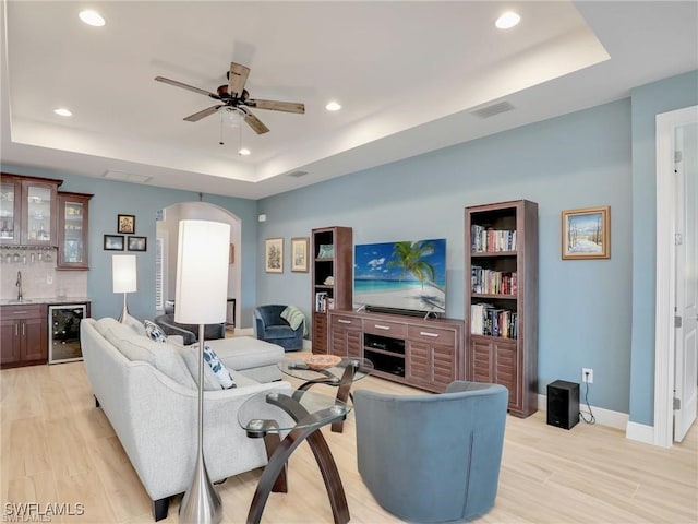 living room with beverage cooler, a raised ceiling, light wood-type flooring, and indoor wet bar