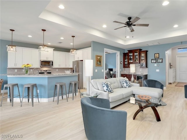 living room with ceiling fan, light hardwood / wood-style floors, a raised ceiling, and sink