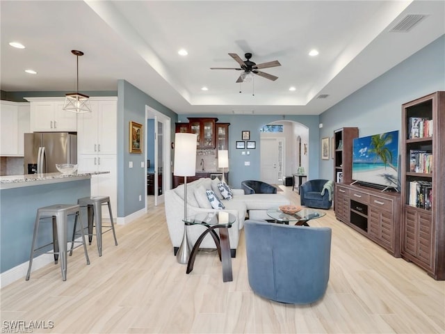 living room featuring light wood-type flooring, ceiling fan, and a tray ceiling