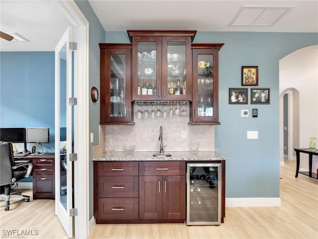 bar featuring light stone countertops, beverage cooler, light wood-type flooring, backsplash, and sink