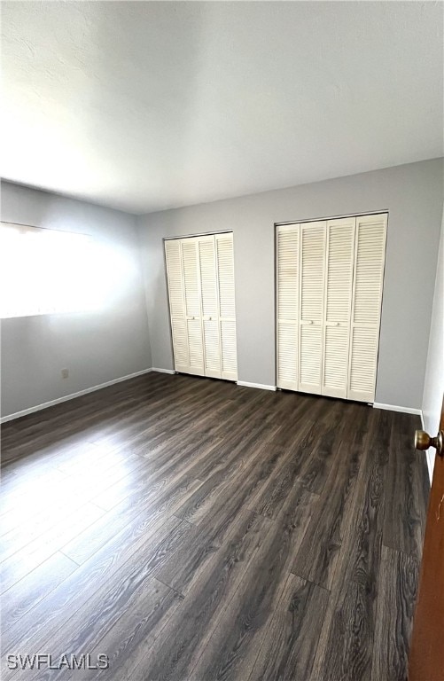 unfurnished bedroom with dark hardwood / wood-style flooring and multiple closets