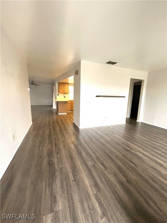 unfurnished living room featuring dark wood-type flooring and ceiling fan