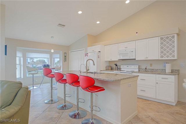 kitchen with lofted ceiling, sink, white appliances, white cabinetry, and an island with sink