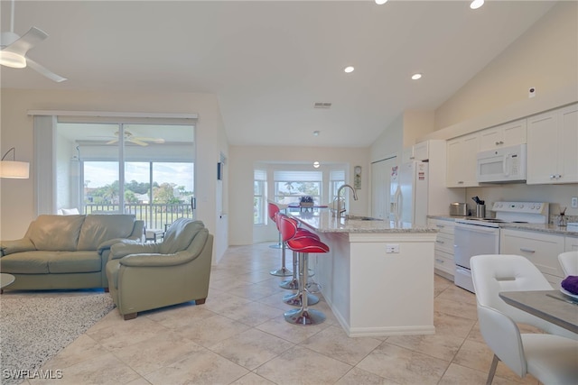 kitchen featuring white cabinetry, a kitchen island with sink, a breakfast bar area, and white appliances