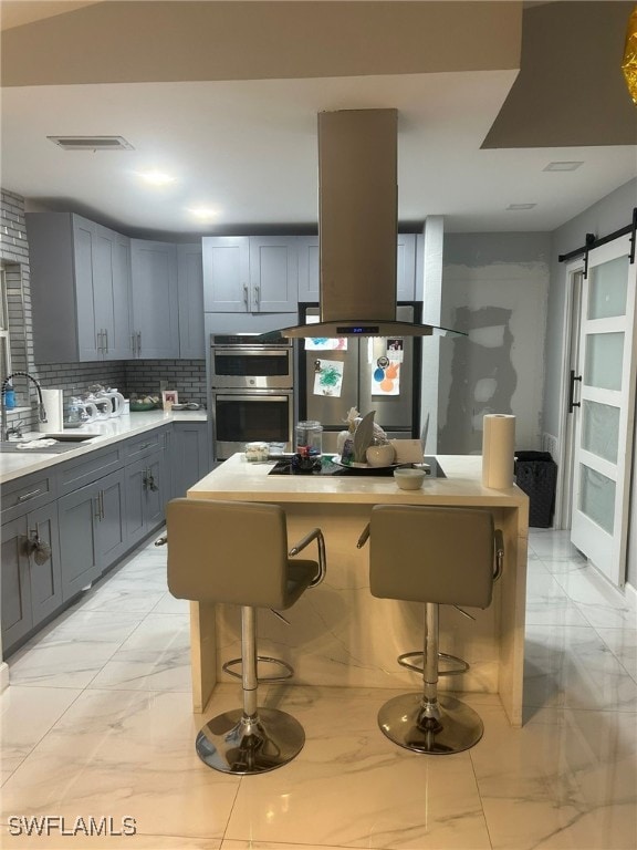 kitchen featuring gray cabinets, a barn door, a breakfast bar area, appliances with stainless steel finishes, and sink