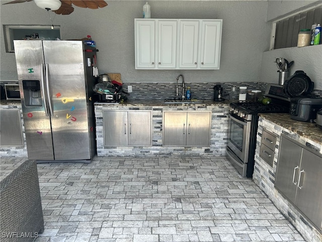 kitchen featuring stainless steel appliances, sink, white cabinetry, dark stone countertops, and backsplash