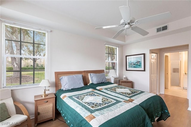 bedroom with light wood-type flooring, ceiling fan, ensuite bath, and multiple windows