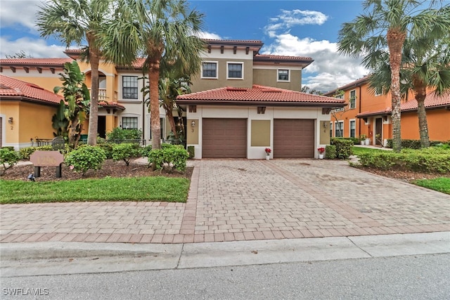 mediterranean / spanish house with a garage, a tiled roof, decorative driveway, and stucco siding